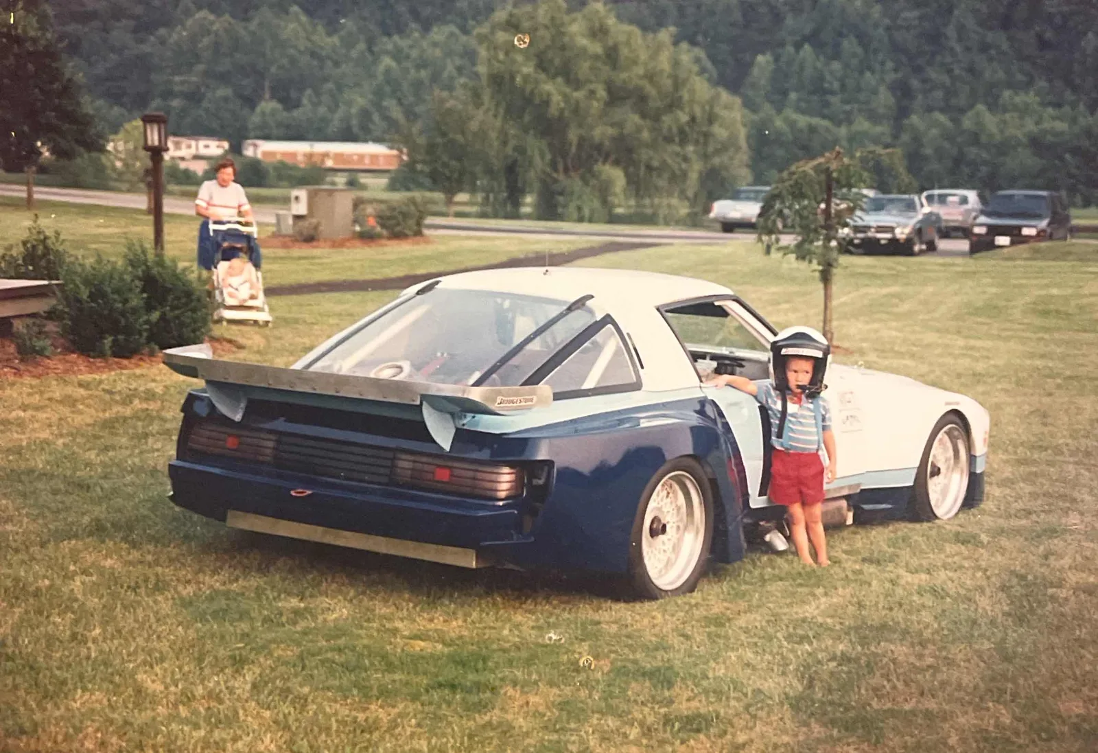 Matt Forbush as a child wearing a helmet beside a blue-and-white race car