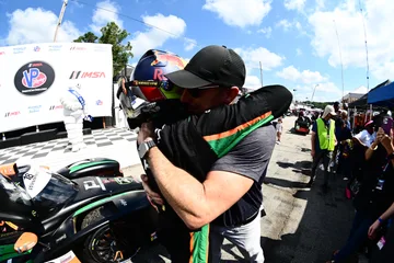 A helmeted Forbush Performance driver and team member embrace beside the car after the Road Atlanta race.