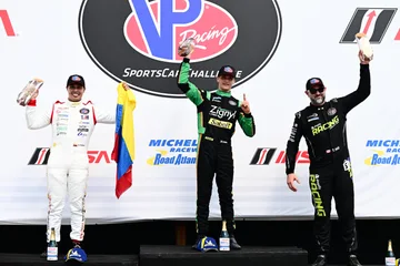 Three drivers raise their trophies on the Road Atlanta podium.