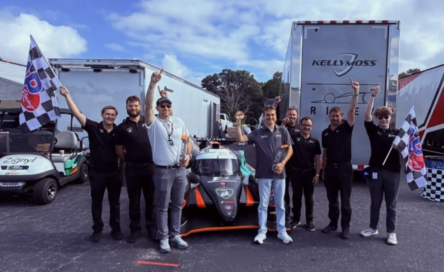 The Forbush Performance team celebrating beside the No. 18 race car with checkered flags